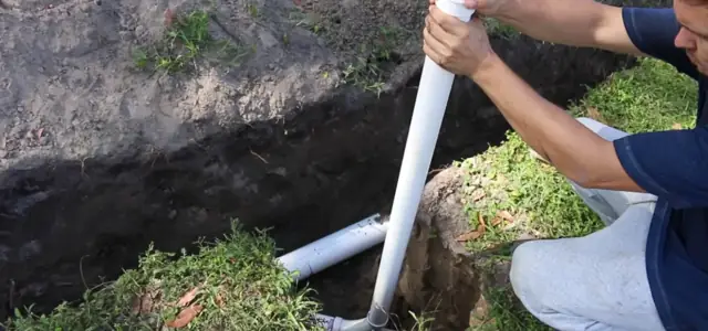 Worker setting white PVC sewer pipe in an open trench in a lawn