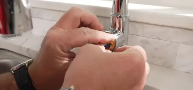 Hands working on the base of a chrome kitchen faucet with a small tool